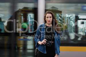 I live to travel. Portrait of an attractive young female photographer standing on the subway with a train passing through in the background.