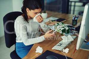 Finding her GPs number in her contacts list. a young businesswoman blowing her nose while texting on a cellphone in an office.