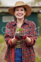 Sustainable farmer holding a plant or seedling outdoors smiling and happy about her organic farm or garden. Young female nature activist that is passionate about sustainability standing on farmland