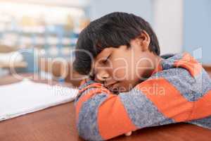 Just a quick nap. a tired elementary school child sleeping on his desk in the classroom.