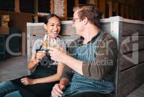 Successful distillery owners relaxing and celebrating with a glass of wine in the cellar or warehouse. Relaxed winemakers or employees enjoying an alcohol drink together at work