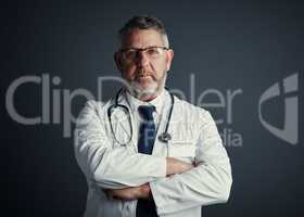 Your health is my only concern. Studio portrait of a handsome mature male doctor standing with his arms folded against a dark background.