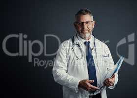 This is my passion. Studio portrait of a handsome mature male doctor holding medical records while standing against a dark background.