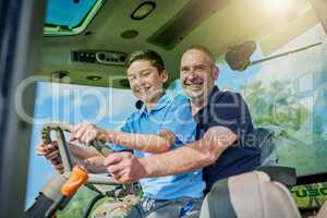 Like father, like son. Low angle portrait of a male farmer and his son inside the cockpit of a modern tractor.