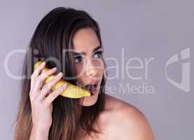 She cant believe her ears. Studio shot of an attractive young woman pretending to use a banana as a phone against a purple background.