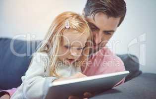 Bonding time in the age of the app. an adorable little girl using a digital tablet with her father on the sofa at home.