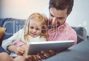 Parenting in the age of digital technology. an adorable little girl using a digital tablet with her father on the sofa at home.