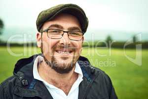 The man of the farm. Portrait of a cheerful young farmer standing on a open green field while looking into the camera outside during the day.