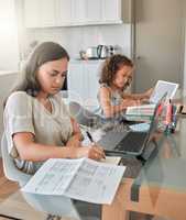 Mother and daughter being productive with remote work and homework, multitasking at a kitchen table at home. Parent and child serious while paying bills and watching an online education programme