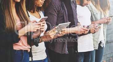 The current way to connect. a group of young people using their wireless devices together outdoors.