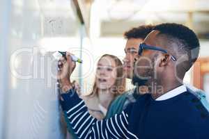 Hell help them pass this semester. a young man writing on a whiteboard while students look on.