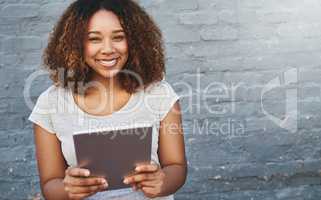 Its the ideal device for me. Portrait of a young woman standing outdoors and using a digital tablet against a gray wall.