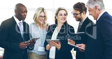 Information exchange. a group of corporate businesspeople standing in a huddle with digital tablets in hand.