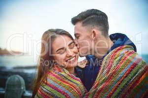 Kisses for my honey bunny. a happy young couple covering themselves with a blanket outdoors.