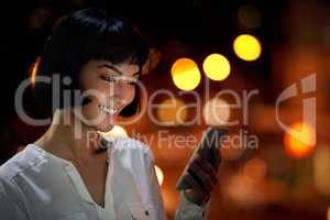 Putting in those overtime hours. an attractive young woman using a mobile phone outside in the city at night.