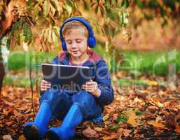 Immersed in technology in the great outdoors. Full length shot of an adorable little boy using a tablet while sitting outdoors during autumn.