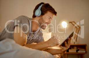 Headphones, digital tablet and in bed watching online movies, videos or series at night in house bedroom. Man on entertainment news or internet film streaming app or website on home 5g wifi network.