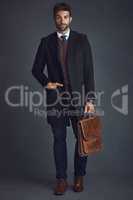 Putting his style to work. Studio portrait of a stylishly dressed young man carrying a bag against a gray background.