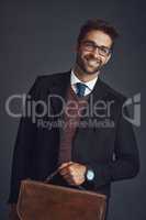 The man of the hour. Studio portrait of a stylishly dressed young man carrying a bag against a gray background.