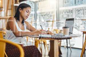 Student writing, taking notes or doing a project assignment in cafe or restaurant using laptop and notebook. Young woman taking an online education class or doing study work, learning in coffee shop.