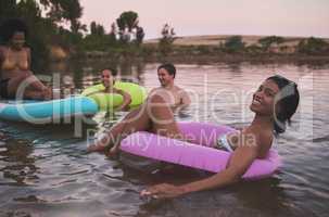 Vacation, swimming and friendship having fun in a lake while enjoying the summer sunset. Happy friends relaxing and floating in water while talking and bonding on a getaway holiday