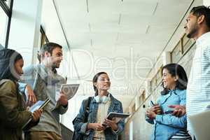 We should organize a study session. Low angle shot of a group of university students talking while standing in a campus corridor.