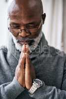 Seeking guidance from above. a handsome senior man praying while sitting in his home.