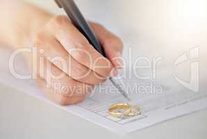 .Woman hand signing legal divorce documents, deal or paper contract in a lawyer office with ring placed on table. Person writing signature on marriage paperwork after agreement at family law office.