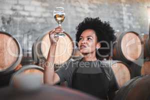 Black woman tasting wine at a winery, looking and checking the color and quality of the years produce. Young African American sommelier proud of the new addition, analyzing white wine in a cellar