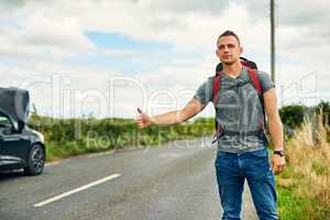 Making a move instead of being left stranded. a young man hitchhiking after having troubles with his car on the road.