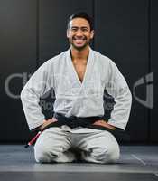 Mma, karate and training with a young man kneeling in a gym, health studio or dojo in his gi or uniform. Portrait of a male training, exercising and learning self defense in a workout and fight class