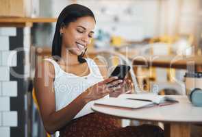 Texting a message or browsing social media on a phone by a young female student sitting in a coffee shop smiling. A relaxed woman relaxing and searching the internet or chatting online at a cafe