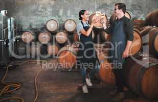 Wine distillery owners cheers glasses in the cellar standing by the barrels. Happy and celebrating business owners or sommeliers enjoying chardonnay or sauvignon blanc inside a winery