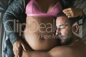 In love with his unborn child. High angle shot of a handsome young man loving his pregnant wife in their bedroom.