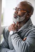 He spends a lot of time deep in thought. a handsome senior man looking contemplative while sitting in his home.