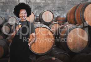 Portrait of a young woman winemaker standing with a glass with wooden barrel of red wine in a winery cellar or distillery. Entrepreneur or business owner working for startup success business success