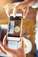 Have to show everyone what Im doing right now. an unrecognizable woman taking a picture of her coffee with a cellphone in a cafe.