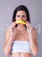 Shes one sad monkey...Studio portrait of an attractive young woman holding a banana against a purple background.