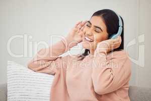 Headphones, listening to music and dancing to fun, happy radio songs while relaxing on home living room sofa. Smiling, cheerful and singing woman having fun and enjoying podcast or dance media sound