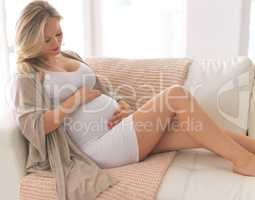 Developing a bond with her unborn baby. a beautiful young pregnant woman sitting on the sofa at home.