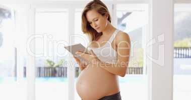 Shes expecting and is researching what to expect. a pregnant woman using a tablet at home.