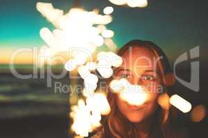 Light up your life. a young woman holding a sparkler at the beach at night.