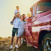 Ready to get on the road. a cheerful family posing for a portrait together outside next to a red pickup truck.