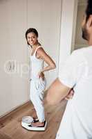 Time to weigh in. a woman weighing herself on a scale while her husband watches at home.