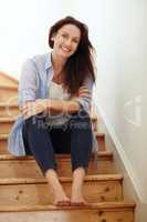 Spending the weekend barefoot on the stairs. a young woman sitting on the staircase at home.