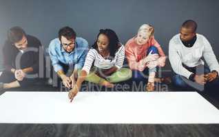 How brilliant ideas are born. Studio shot of a group of people sitting on the floor and working on blank paper against a gray background.