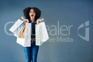 Payday shopping mania. Studio portrait of a young woman carrying shopping bags and looking surprised against a blue background.