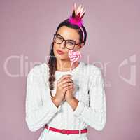 No one is too old for fairytales. a young woman posing with a party crown and a lollipop against a pink background.