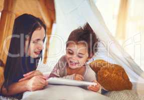 Getting cozy with their favourite gadget. a mother and her little daughter using a digital tablet together at home.