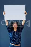 Lets put your message at the top. Studio shot of a young woman holding up a blank placard against a blue background.